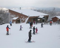 Skiers head towards the Saddle Mid-Mountain Lodge with views of the Adirondack High Peaks in the background Skiers head towards the Saddle Mid-Mountain Lodge with views of the Adirondack High Peaks in the background