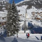 Skiers descend into a mountain village on the Sella Ronda tour as a local church and alpine homes form the setting in the Dolomites Sella Ronda Mountain Village and Church